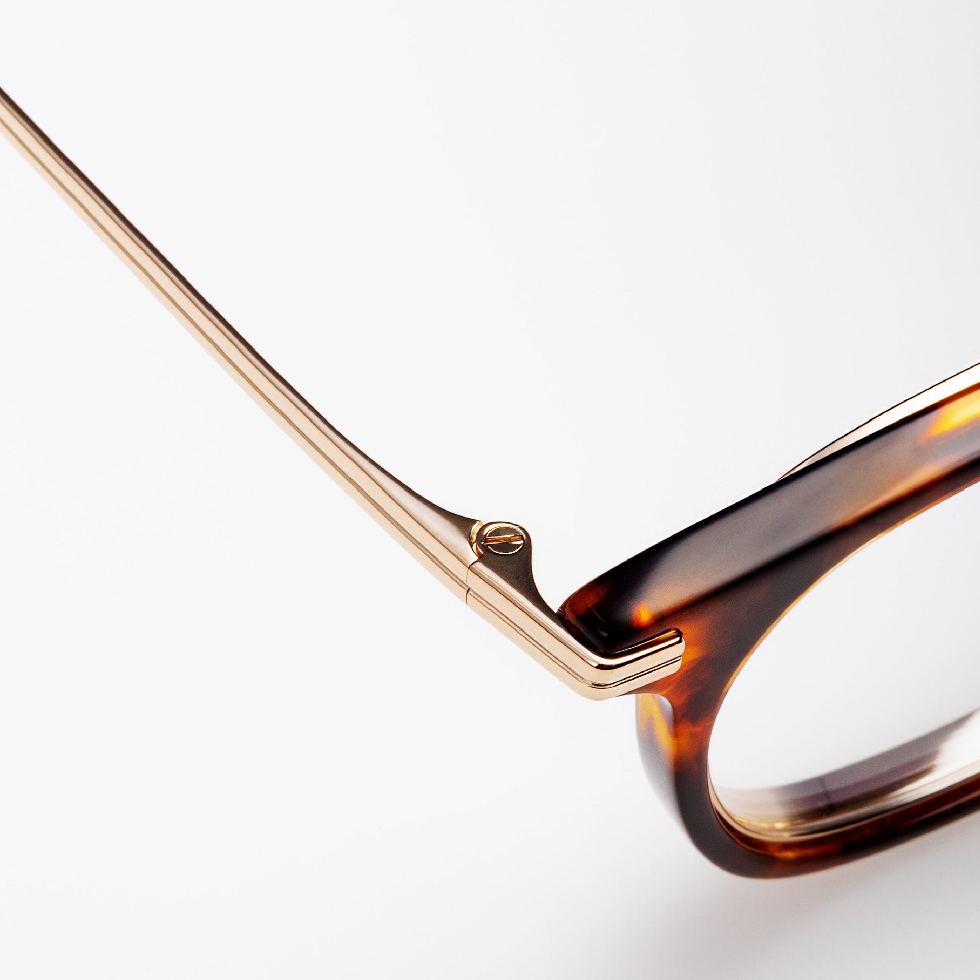 Close-up of a pair of glasses with a gold frame and tortoiseshell lenses on a white background.